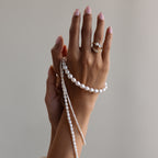 A hand with pink nails, rings, and pearls wrapped around the wrist against a neutral background highlights the modern Summer Pearl Beaded Necklace.