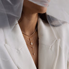 Woman in a white blazer wears the Leena Diamond Lariat Necklace layered with gold chains and a sheer white veil.