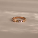 The Multiple Birthstone Band in Rose Gold features four square gemstones in yellow, green, white, and pink on a beige surface—a beautiful personalized jewelry piece and perfect mothers gift.