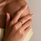 A hand wearing the Multiple Birthstone Band, set with blue stones, rests gently on a bare shoulder.