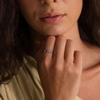 A woman with wavy hair showcases the Multiple Birthstone Band on her finger, hand near her chin—a stunning personalized jewelry piece.