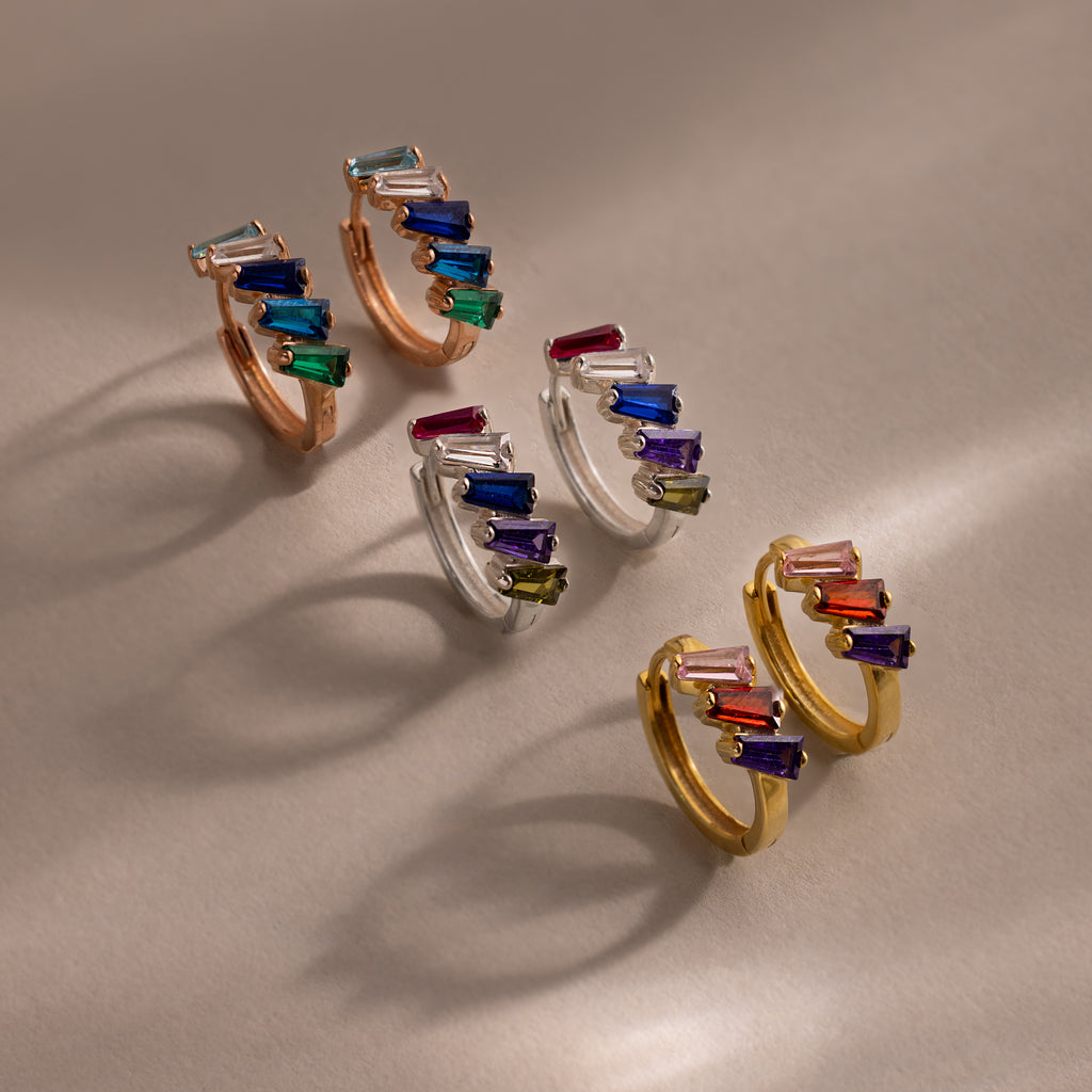 Multiple Tapered Birthstone Huggies: Three pairs of hoop earrings in gold, silver, and rose gold, featuring colorful tapered birthstones in an Art Deco-inspired modern statement design.