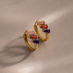 Multiple Tapered Birthstone Huggies in 18K Gold feature pink, red, and purple rectangular gemstones for a modern statement look against a soft beige background.
