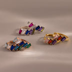 The Multiple Tapered Birthstone Huggies in Rose Gold showcase vibrant gemstones set in rose gold hoops, inspired by Art Deco design and displayed on a soft beige background.