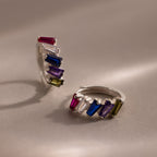 The Multiple Tapered Birthstone Huggies in Sterling Silver feature two silver hoops adorned with tapered gemstones in pink, white, blue, purple, and green—ideal for adding a playful art deco flair to any look.