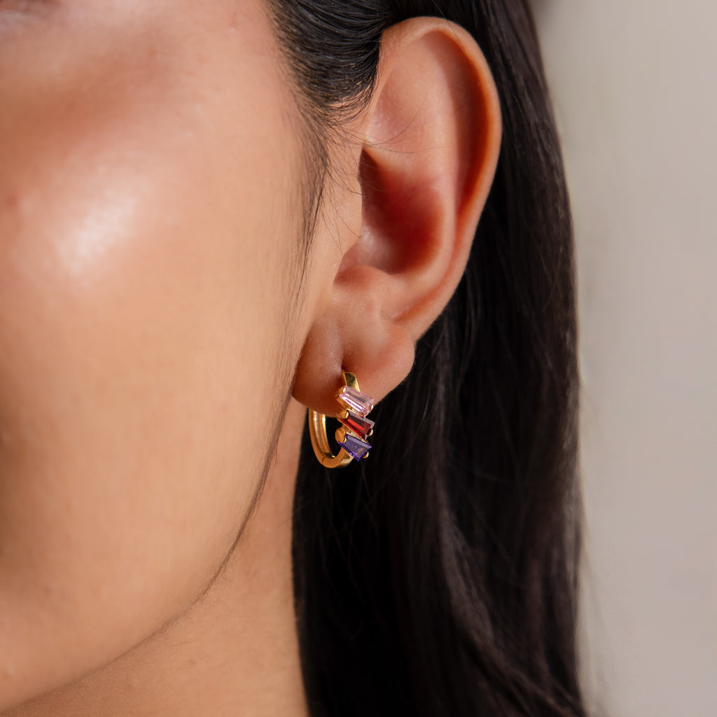 Close-up of a woman's ear wearing Multiple Tapered Birthstone Huggies in rose gold, adorned with red and purple stones.