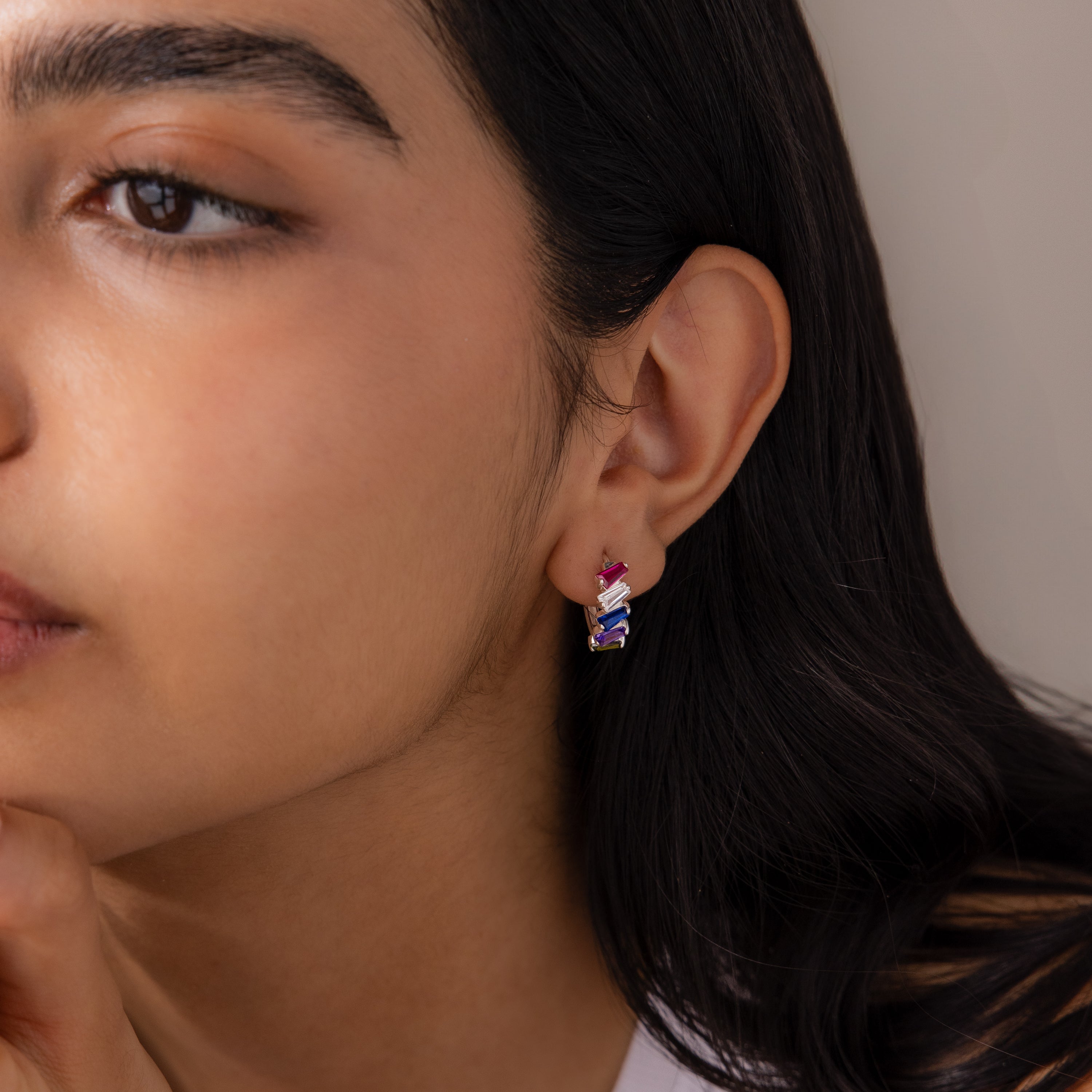 A woman with long dark hair wears Multiple Tapered Birthstone Huggies in Sterling Silver on her left ear.