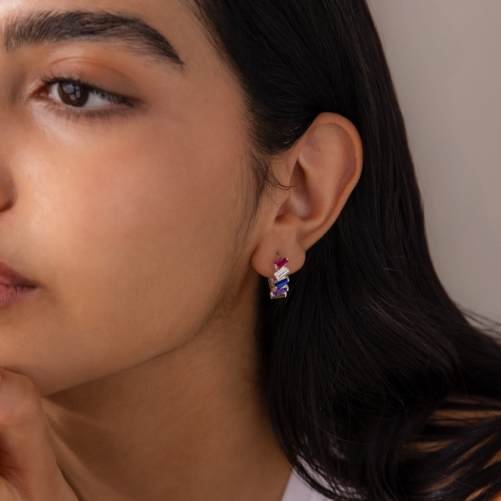 Close-up of a woman wearing Multiple Tapered Birthstone Huggies with pink and purple accents on her left ear, adding a modern statement touch to her style.