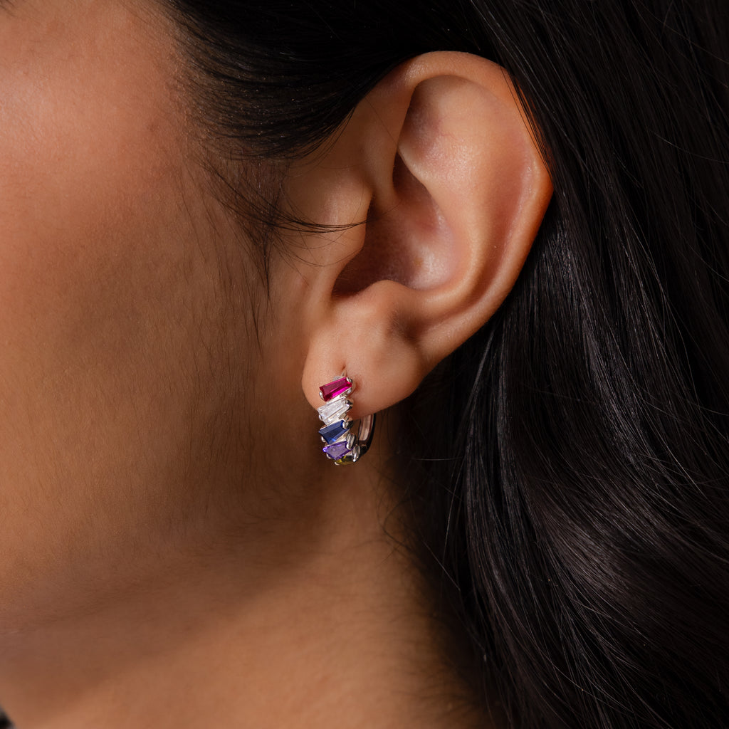 Close-up of a woman’s ear wearing Multiple Tapered Birthstone Huggies in Sterling Silver, featuring vibrant gemstones that add a touch of art deco style.
