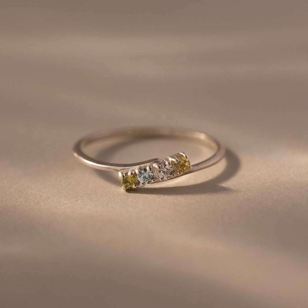 A delicate sterling silver stacking ring featuring three small gemstones in green, blue, and yellow—a beautiful Multiple Birthstone Curve Ring in Sterling Silver for personalized jewelry lovers.