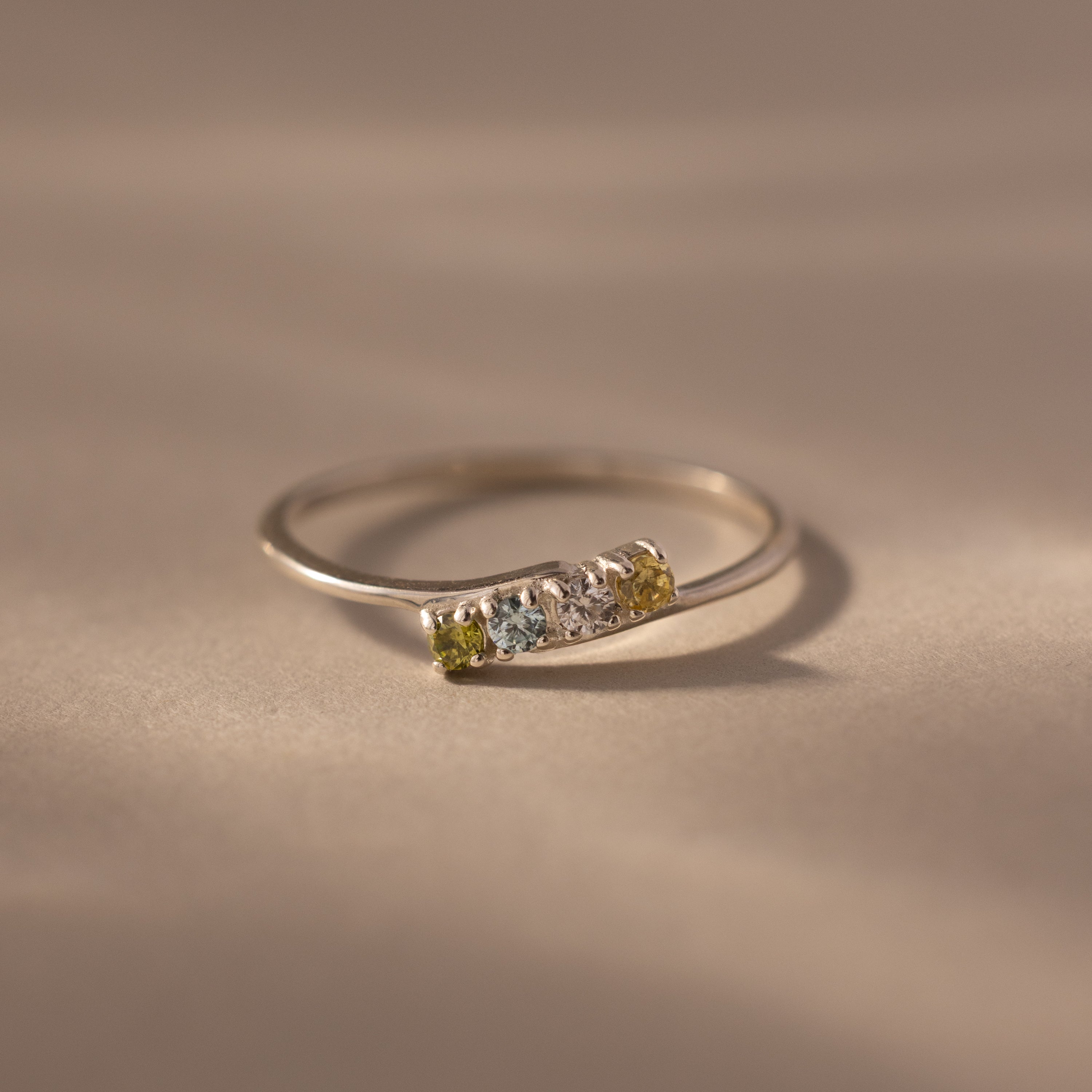 A delicate sterling silver stacking ring featuring three small gemstones in green, blue, and yellow—a beautiful Multiple Birthstone Curve Ring in Sterling Silver for personalized jewelry lovers.