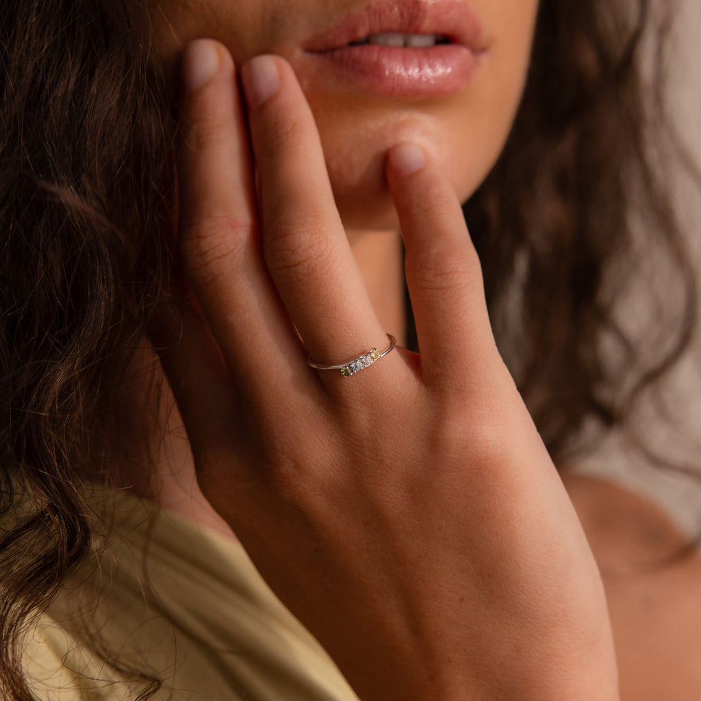 A woman with curly hair touches her face, highlighting the Multiple Birthstone Curve Ring in Sterling Silver on her finger.