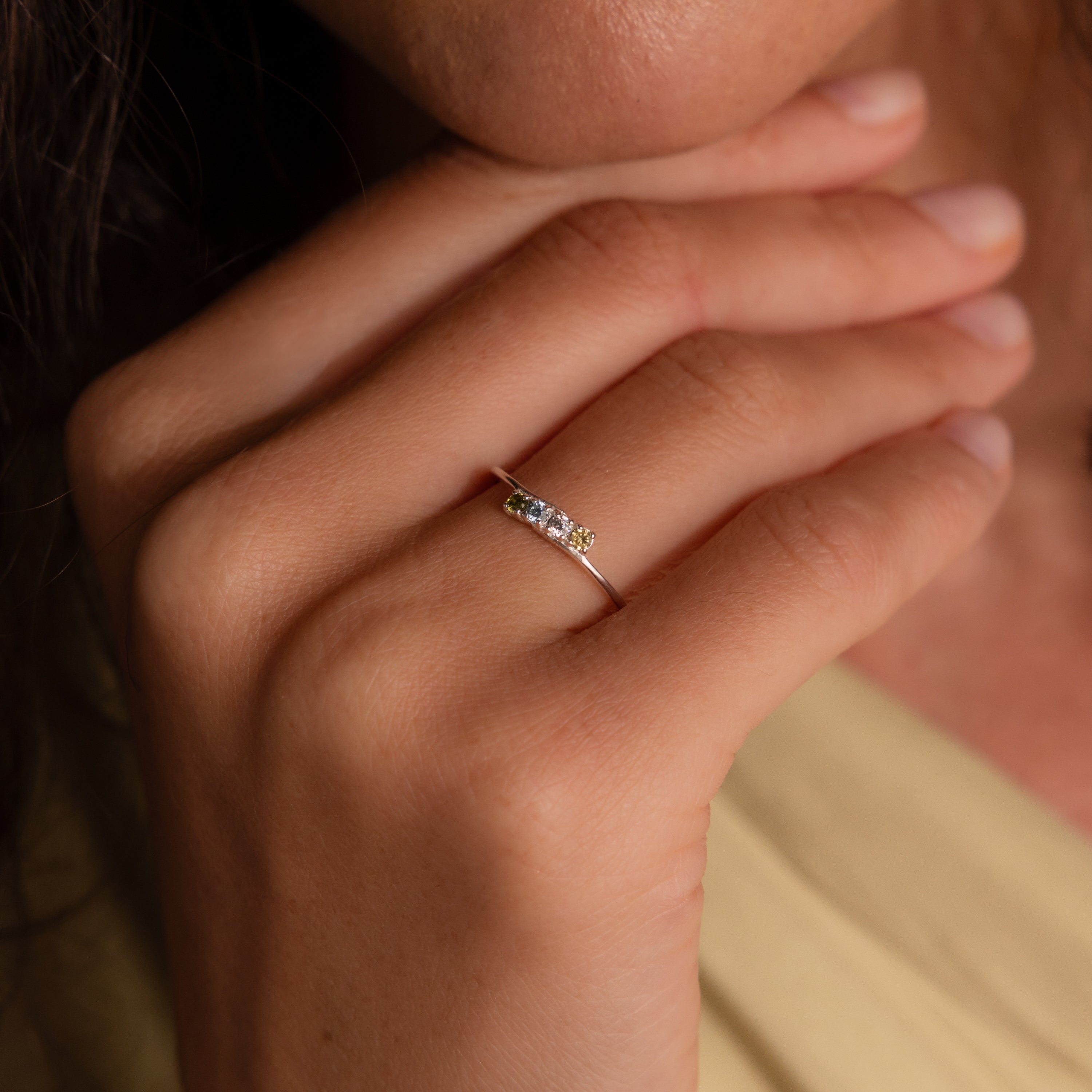 A close-up of a hand wearing the Multiple Birthstone Curve Ring in Sterling Silver, showcasing three small gemstones on the ring finger—a beautiful piece of personalized jewelry.