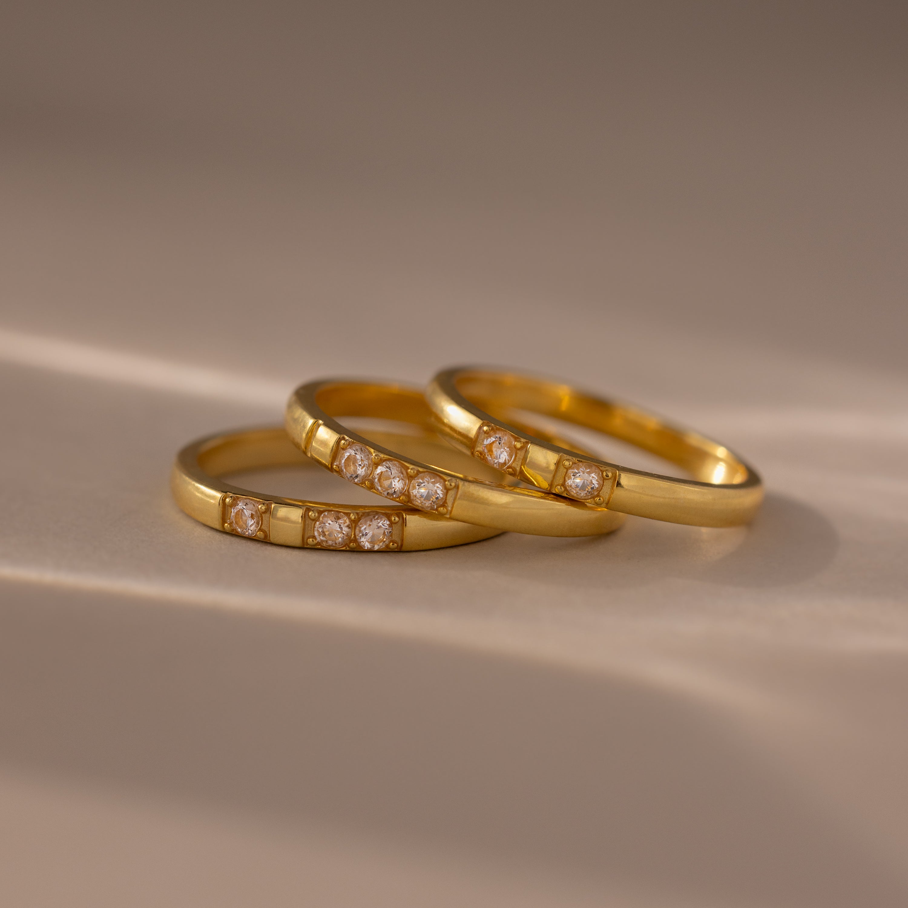 Three Diamond Morse Code Rings in 18K gold are stacked together on a smooth, light surface with soft lighting, forming a meaningful jewelry set that resembles a hidden message ring.