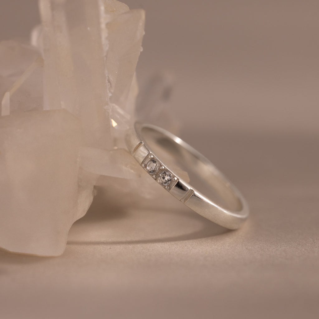 The Diamond Morse Code Ring in Sterling Silver, featuring three small diamonds, rests against a cluster of clear crystals.