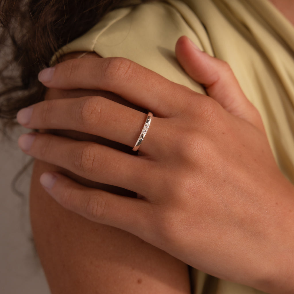 A hand with neatly manicured nails wears the Diamond Morse Code Ring in Sterling Silver, its delicate stones forming a hidden message as it rests gently on a shoulder.