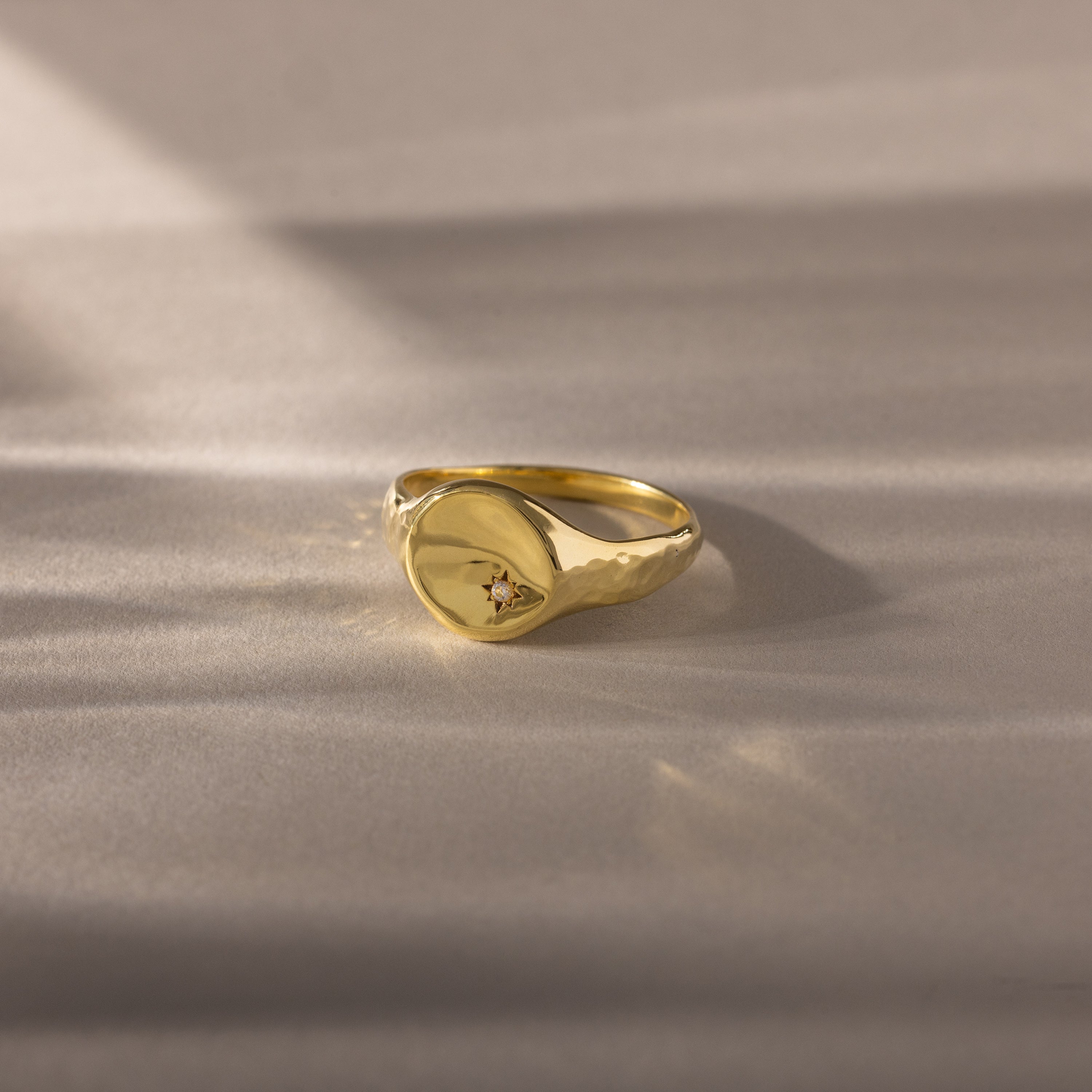 The North Star Birthstone Signet Ring in Diamond (April) features a round, flat top with a diamond accent, shown on a soft beige surface—an elegant and symbolic jewelry piece.