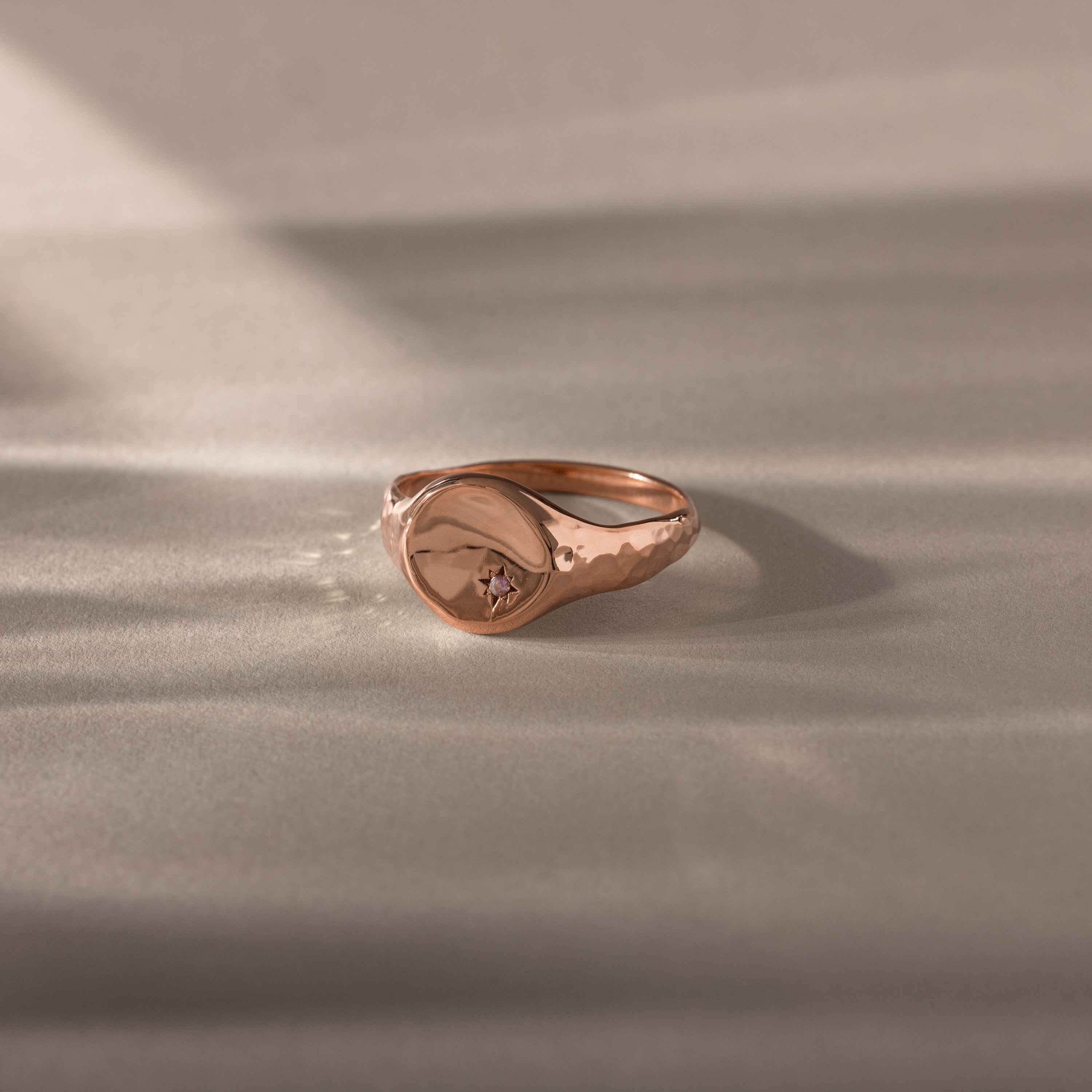 The North Star Alexandrite Signet Ring in rose gold features a small star-shaped alexandrite gem, resting on a soft, light surface—a symbolic jewelry piece that shines with subtle elegance.