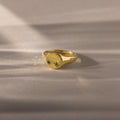 The North Star Birthstone Signet Ring in emerald (May) features a small green gemstone at its center and is showcased on a soft beige surface.