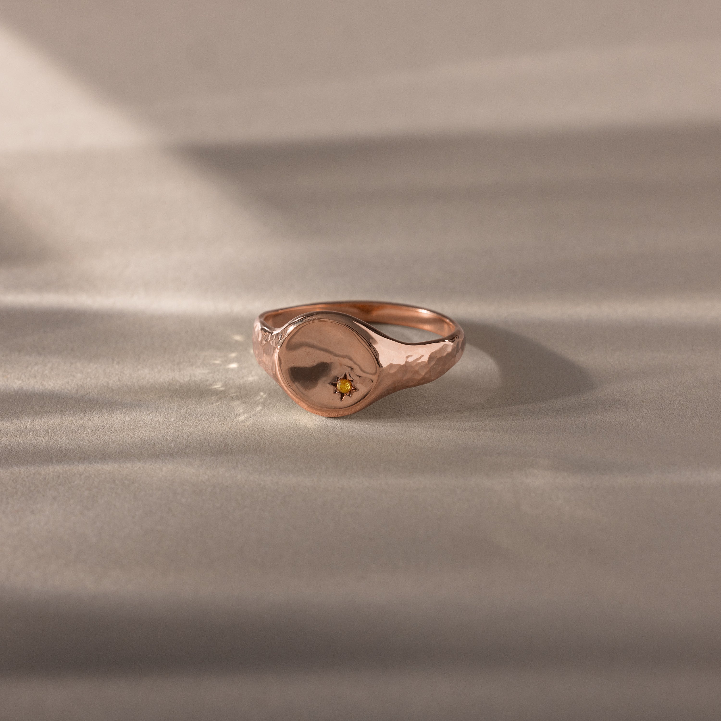 The North Star Topaz Signet Ring, featuring a small engraved star, rests on a softly lit beige surface, showcasing vintage-inspired charm and timeless symbolic jewelry appeal.