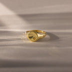 The North Star Birthstone Signet Ring in Topaz (November) features a small star-shaped engraving and is displayed on a soft, beige surface.