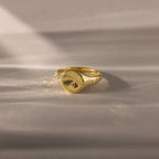 The North Star Birthstone Signet Ring in garnet, a symbolic gold piece for January birthdays, rests on a soft beige surface.