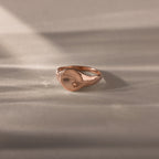 The North Star Pink Tourmaline Signet Ring, featuring a delicate star-shaped detail, rests on a softly lit surface and captures the essence of symbolic jewelry.