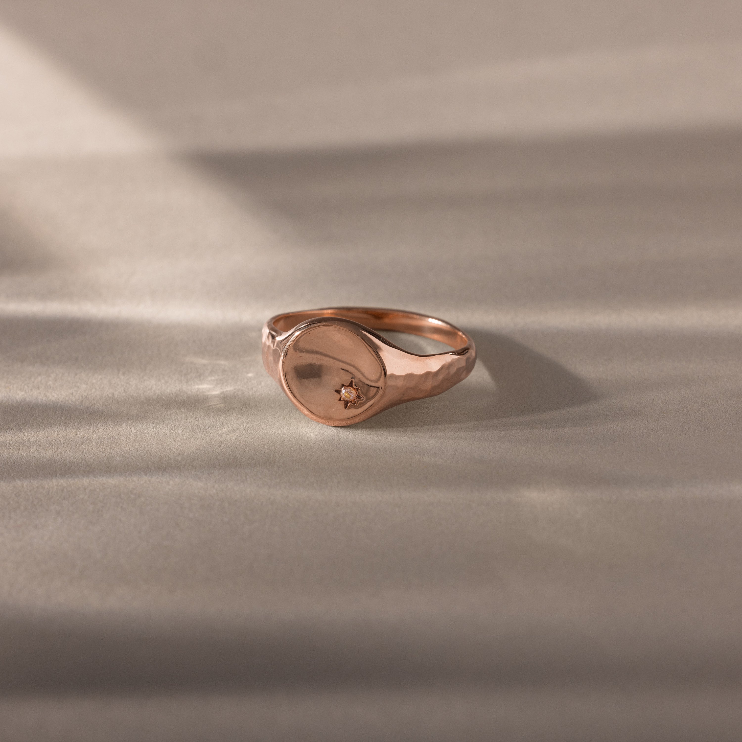 The North Star Pink Tourmaline Signet Ring, featuring a delicate star-shaped detail, rests on a softly lit surface and captures the essence of symbolic jewelry.