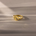 North Star Sapphire Signet Ring featuring a small blue stone, displayed on a soft beige surface with gentle shadows—a timeless piece of symbolic jewelry perfect for daily wear.