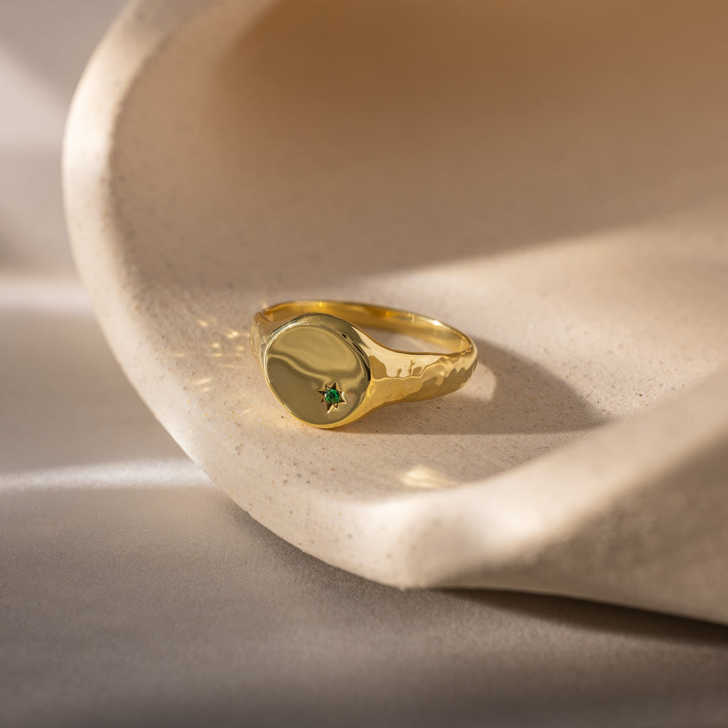 The North Star Emerald Signet Ring, featuring a small green gemstone, rests on a curved beige stone—an elegant and symbolic jewelry piece ideal for meaningful gifts.