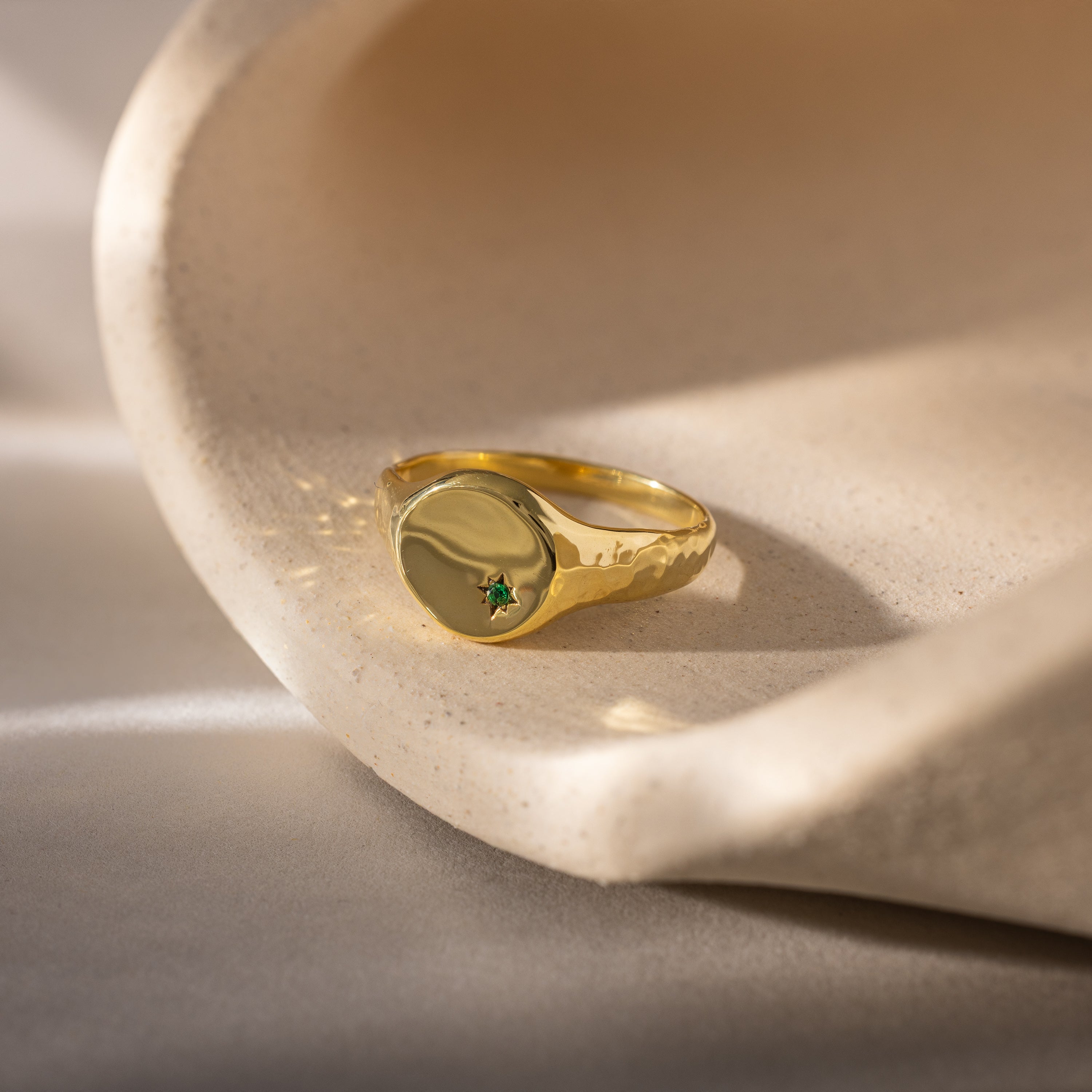 The North Star Emerald Signet Ring, featuring a small green gemstone, rests on a curved beige stone—an elegant and symbolic jewelry piece ideal for meaningful gifts.
