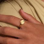 A hand wearing the North Star Birthstone Signet Ring with a small green gemstone on the index finger—this elegant piece adds a touch of sophistication and personal significance.