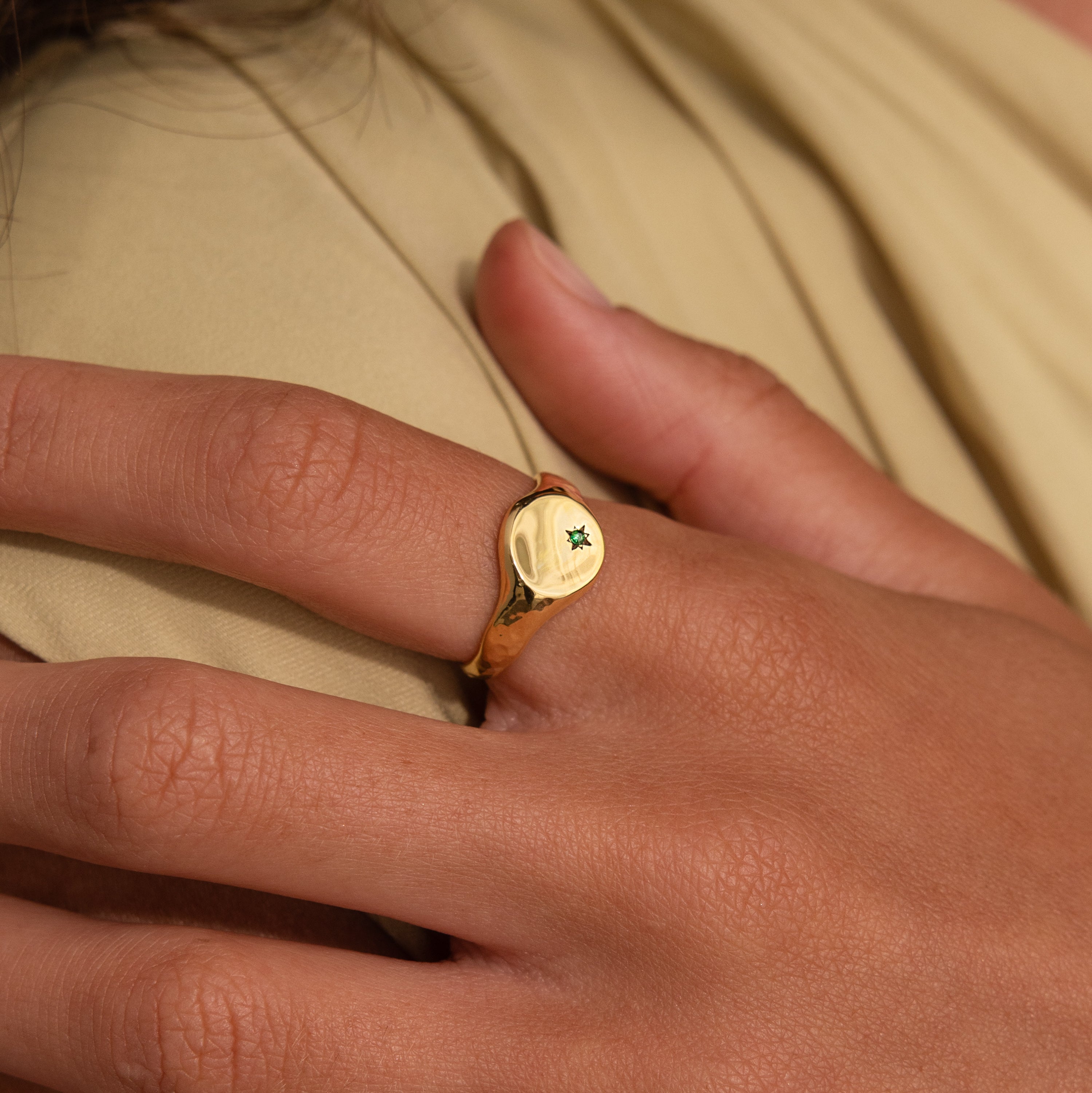 A hand wearing the North Star Birthstone Signet Ring with a small green gemstone on the index finger—this elegant piece adds a touch of sophistication and personal significance.
