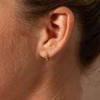 Close-up of a person’s ear wearing Ribbed Emerald Huggies—small gold hoop earrings with a single emerald gemstone. A perfect, meaningful gift for any occasion.