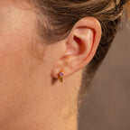 Close-up of a persons ear wearing gold Ribbed Alexandrite Huggies, featuring a pink gemstone for a stylish look.