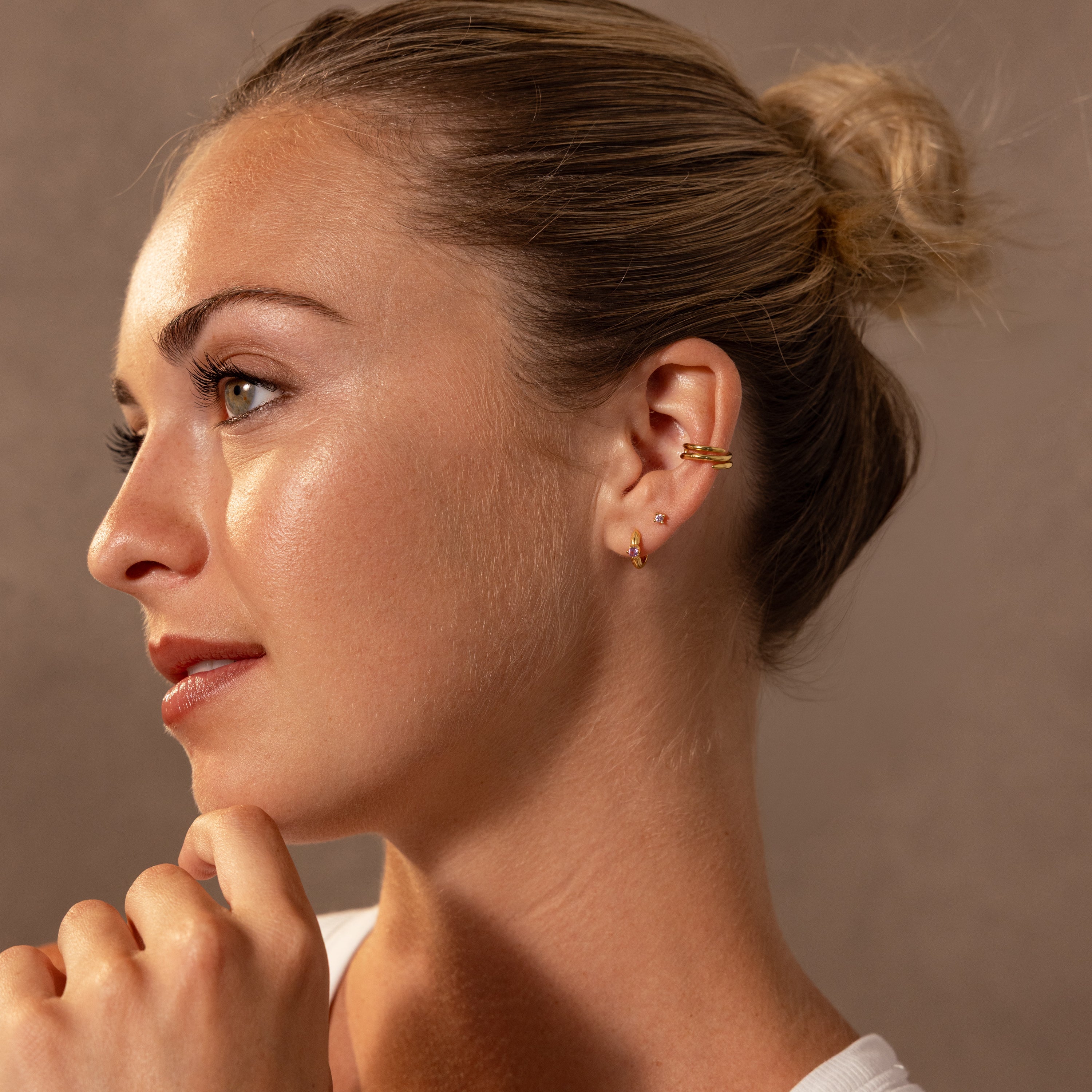 Woman with blonde hair in a bun, wearing Ribbed Alexandrite Huggies, looking to the left against a neutral background.