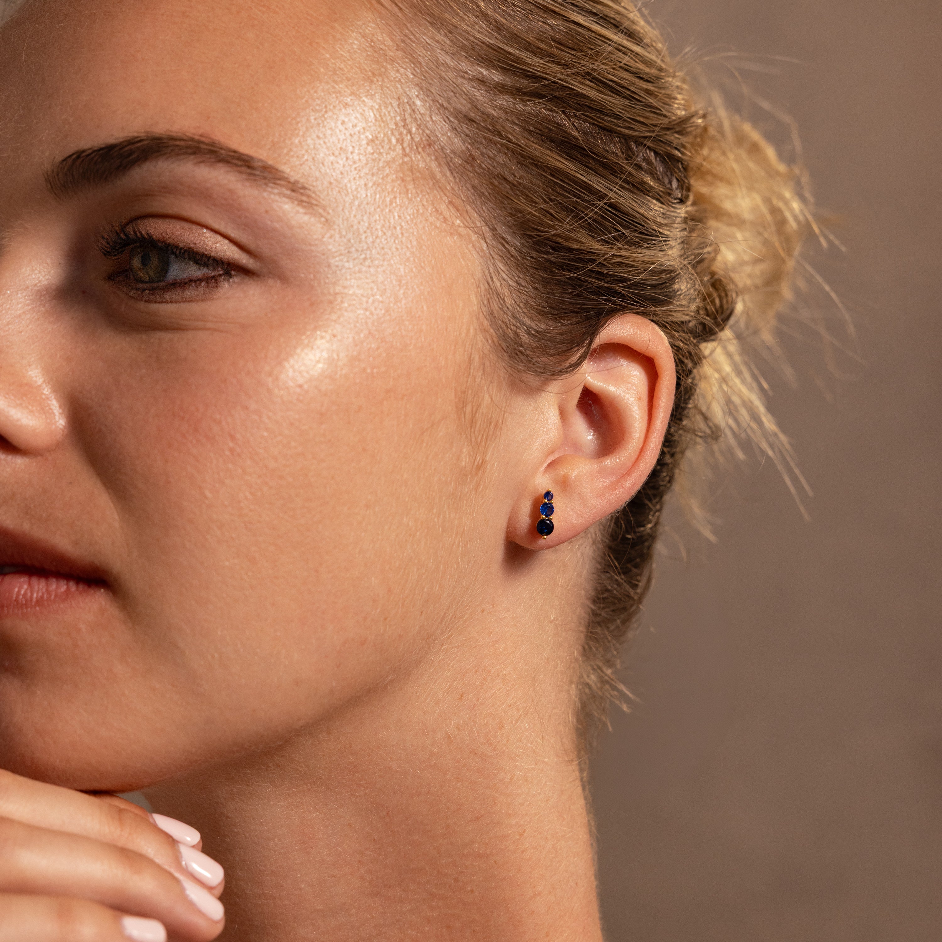 A woman with glowing skin wears elegant Ombre Sapphire Flatback Studs and has her hair in a loose bun.