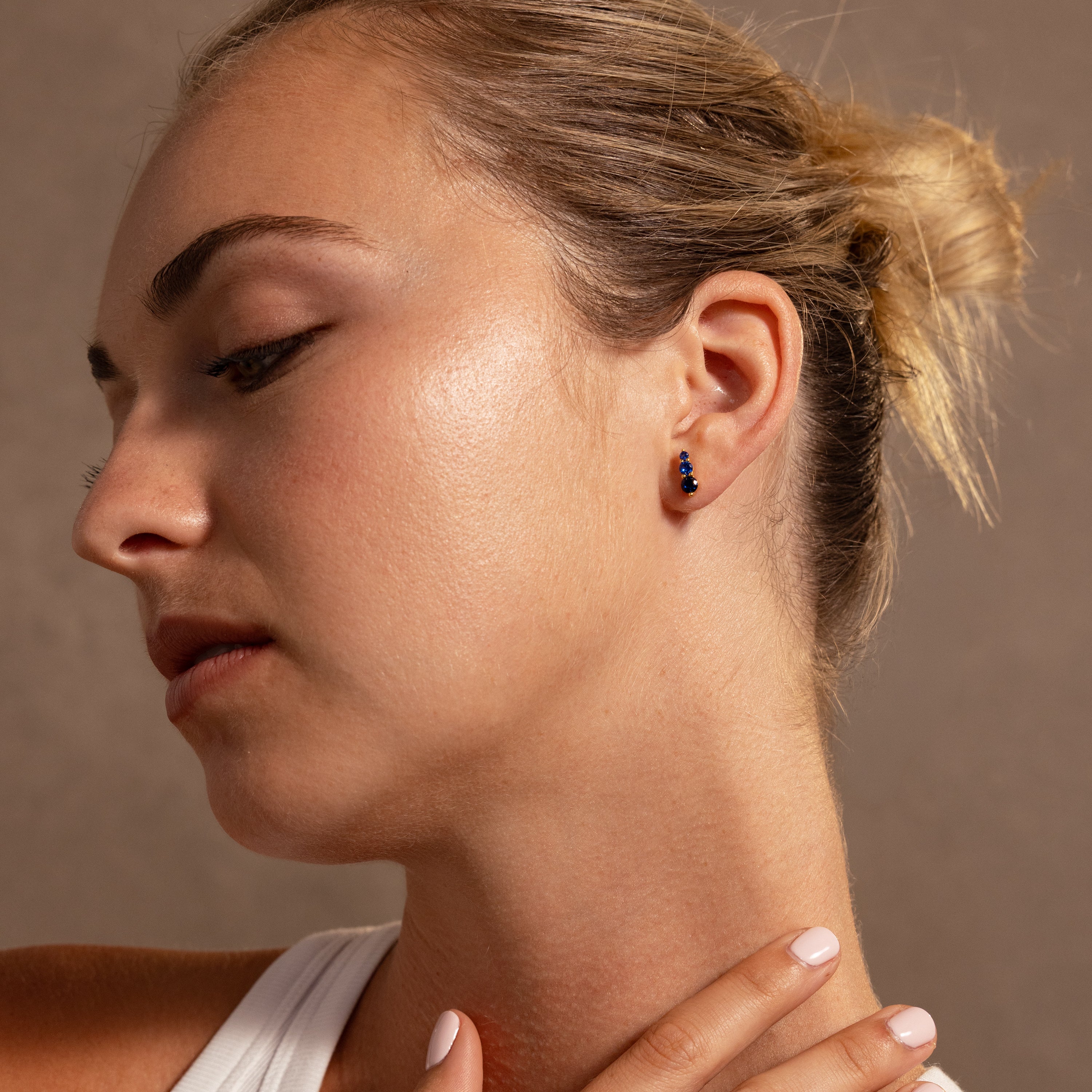 Woman with blonde hair in a bun wearing a white top and Ombre Blue Zircon Flatback Studs, looking down to the side—an ideal choice for a personalized gift.
