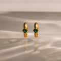 Ribbed Emerald Huggies stand upright on a reflective, softly lit surface—perfect as gold hoop earrings with green gemstones for a meaningful gift.