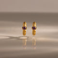 A pair of Ribbed Pink Tourmaline Huggies with pink gemstones, standing upright on a reflective surface—gold hoop earrings that make a meaningful gift.
