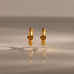 A pair of Ribbed Topaz Huggies gold hoop earrings with yellow gemstones displayed on a reflective, neutral surface.