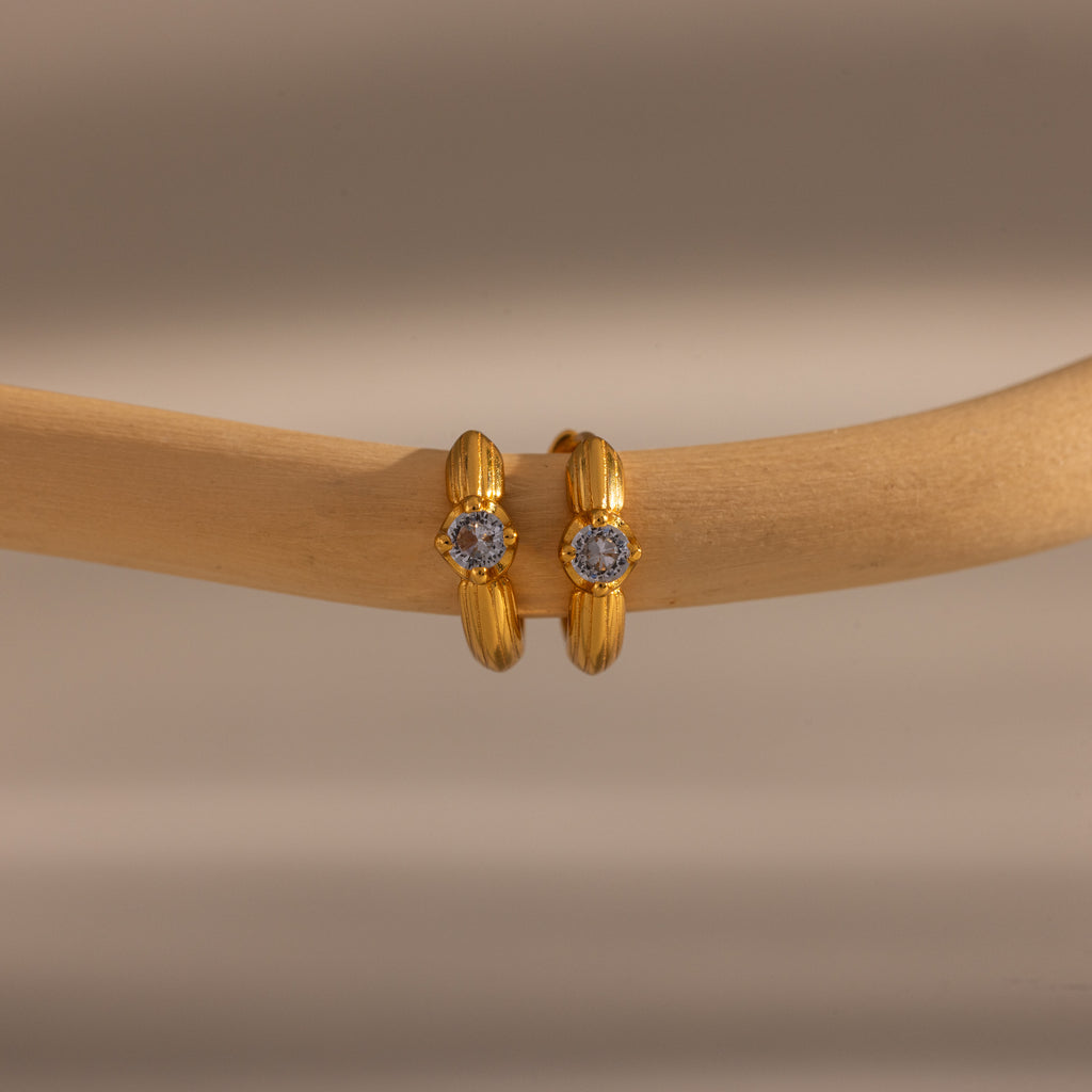 Small gold hoop earrings with a central emerald, displayed on a smooth wooden branch—these Ribbed Emerald Huggies make a meaningful gift for any occasion.