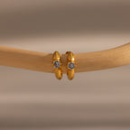 Small gold hoop earrings with a central emerald, displayed on a smooth wooden branch—these Ribbed Emerald Huggies make a meaningful gift for any occasion.