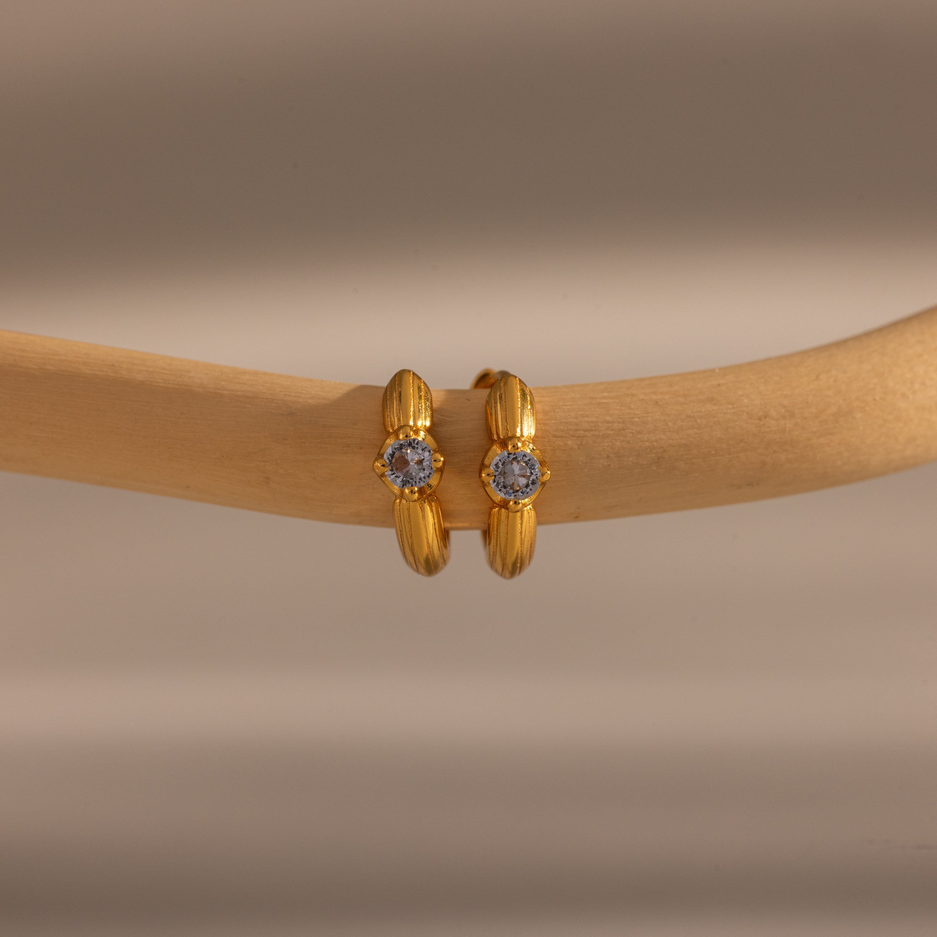 Small gold hoop earrings with a central emerald, displayed on a smooth wooden branch—these Ribbed Emerald Huggies make a meaningful gift for any occasion.