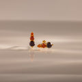 Ombre Garnet Flatback Studs featuring three orange and dark gemstones on a glossy surface with soft lighting—ideal as vibrant earrings or a personalized gift.