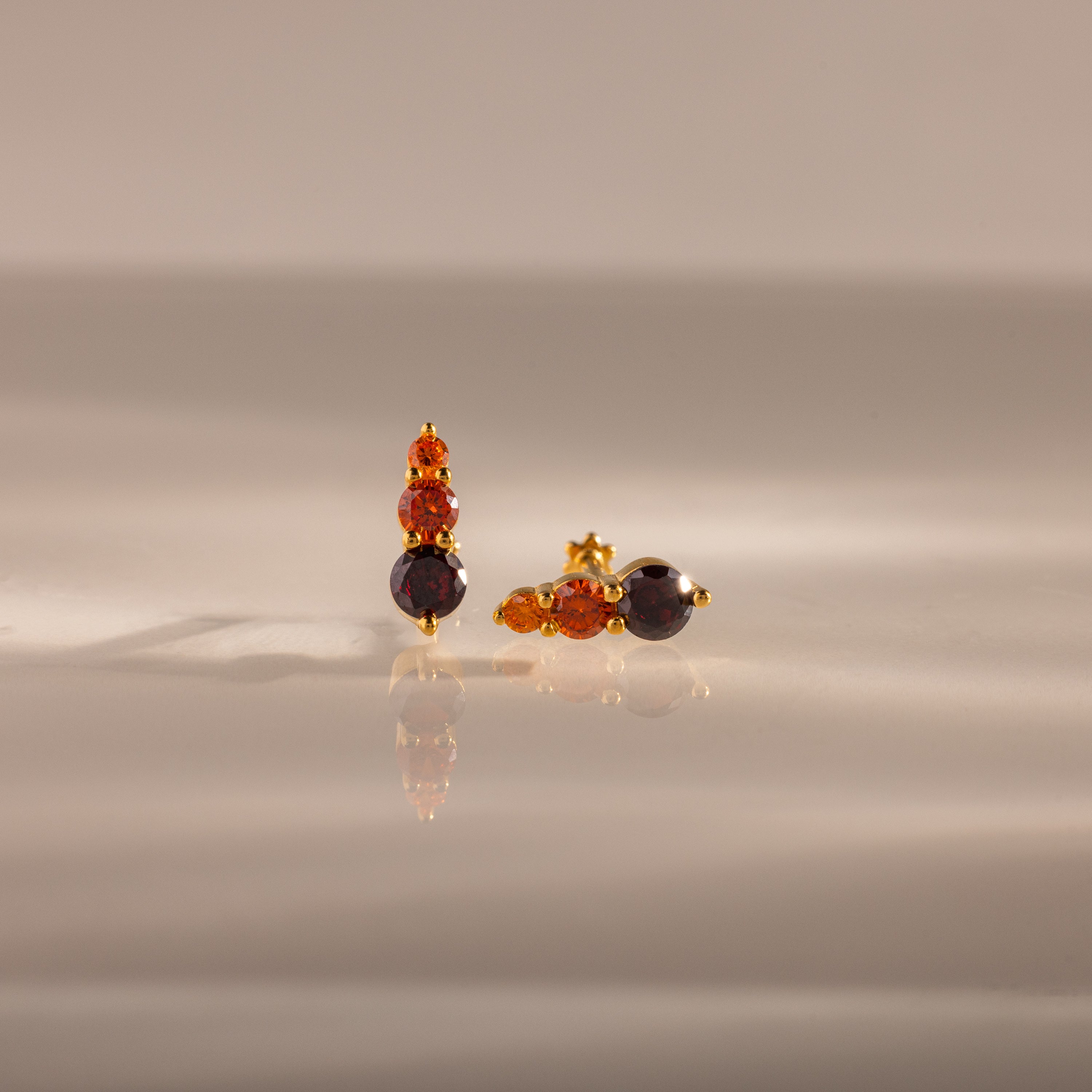 Ombre Garnet Flatback Studs featuring three orange and dark gemstones on a glossy surface with soft lighting—ideal as vibrant earrings or a personalized gift.