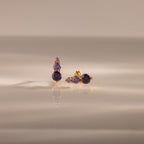 Ombre Amethyst Flatback Studs feature gold earrings with three stacked purple gemstones, shown on a smooth, reflective surface—ideal as a personalized gift or stylish flatback studs.