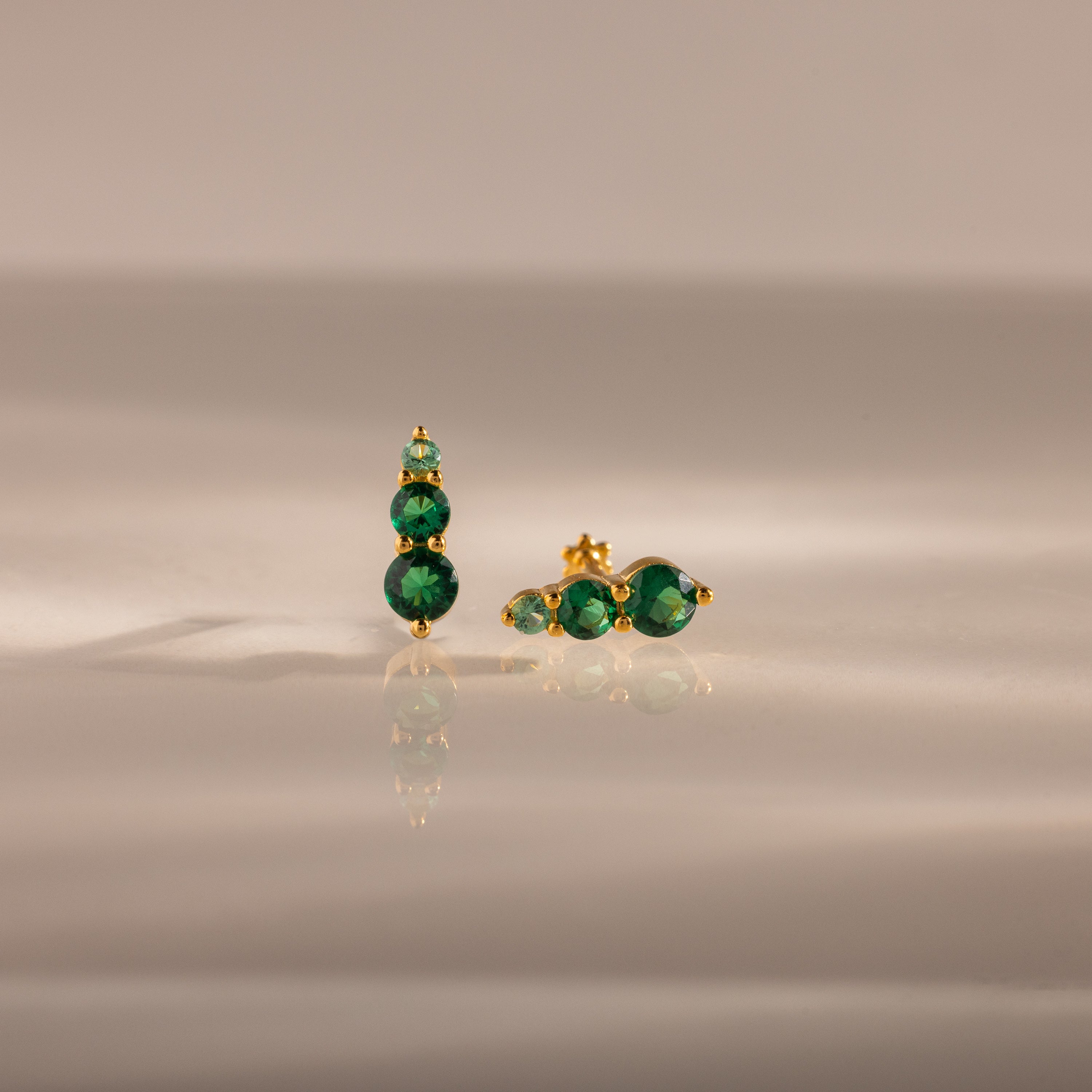 Ombre Emerald Flatback Studs with three round green gemstones on gold, shown on a smooth neutral surface—an elegant pick for fans of personalized jewelry.