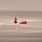 Ombre Birthstone Flatback Studs in Ruby (July) with three round pink gemstones rest on a reflective beige surface—ideal as personalized birthstone jewelry.