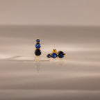 Ombre Sapphire Flatback Studs featuring three blue gemstones on a smooth, reflective beige surface—elegant, personalized jewelry for any occasion.